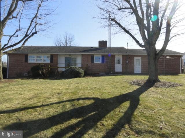 ranch-style house with brick siding, a chimney, and a front lawn