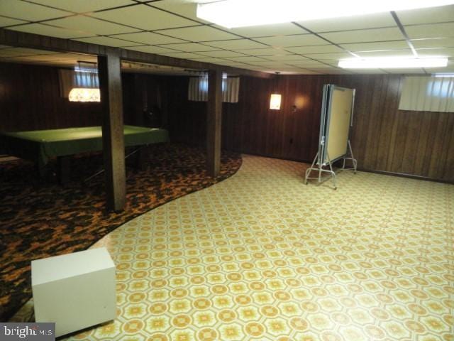 finished below grade area with tile patterned floors, a paneled ceiling, and wood walls