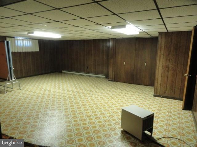 finished basement featuring a baseboard heating unit, wooden walls, and light floors