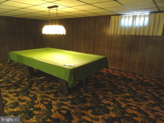 recreation room featuring a paneled ceiling, wooden walls, and carpet floors