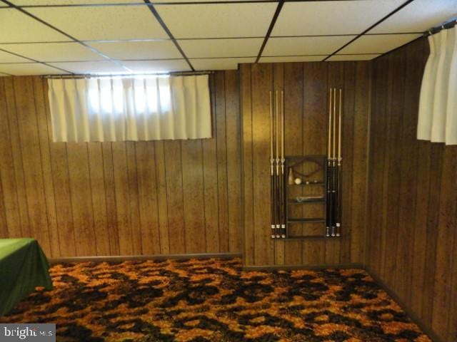 below grade area with a paneled ceiling and wood walls