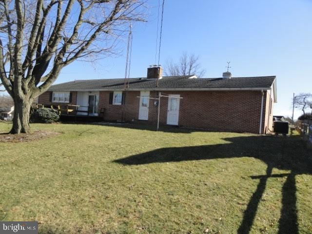 back of house with central air condition unit, a lawn, a chimney, and brick siding