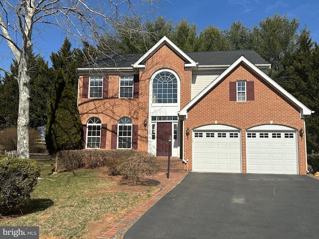 colonial inspired home with aphalt driveway, an attached garage, brick siding, and roof with shingles