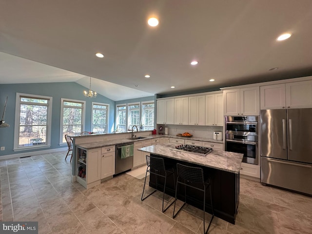 kitchen featuring a sink, light stone counters, white cabinetry, stainless steel appliances, and lofted ceiling