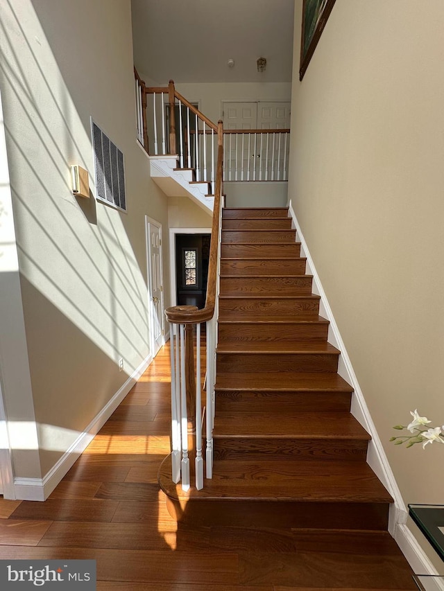 stairs with visible vents, a towering ceiling, baseboards, and wood-type flooring