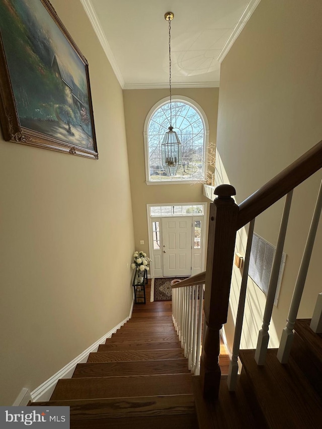 stairs featuring wood finished floors, baseboards, a towering ceiling, and ornamental molding