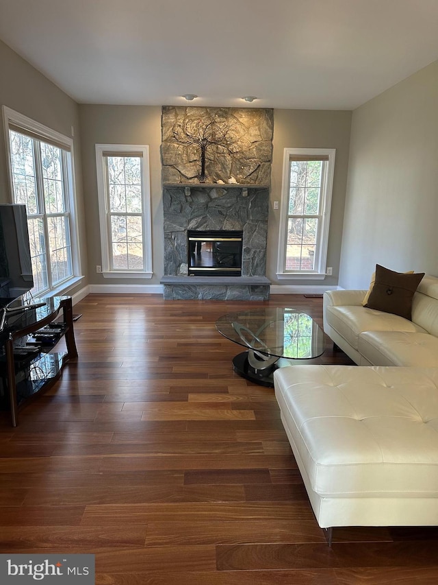 living area with a stone fireplace, baseboards, and wood finished floors