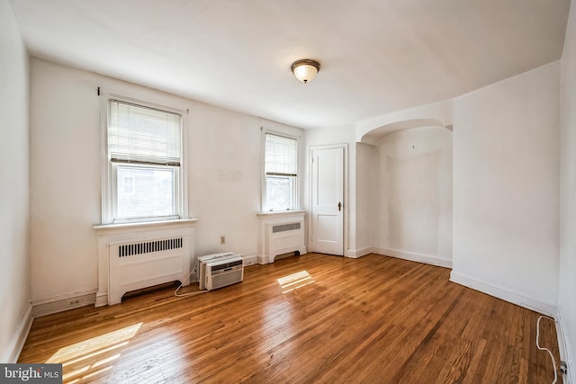 spare room featuring radiator heating unit, arched walkways, baseboards, and wood finished floors