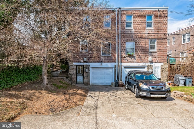 rear view of house featuring fence, an attached garage, brick siding, and concrete driveway