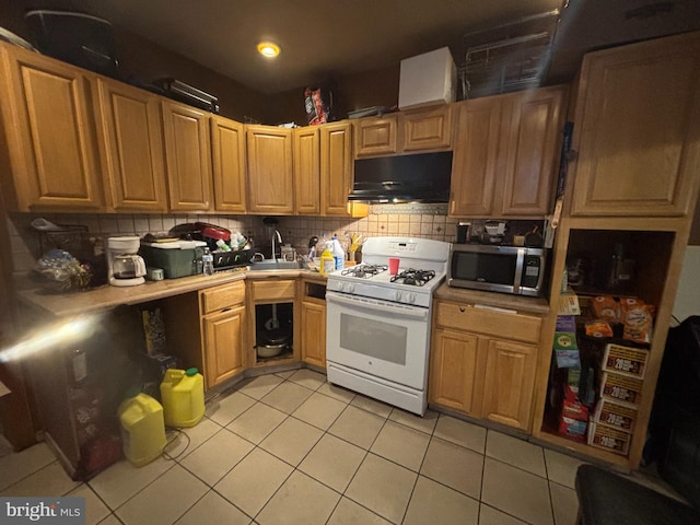 3316 Jasper St, Philadelphia, PA 19134 - kitchen with white range with gas stovetop, light tile patterned flooring, decorative backsplash, under cabinet range hood, and stainless steel microwave