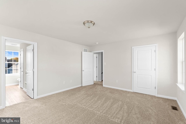 unfurnished bedroom with visible vents, baseboards, light colored carpet, and ensuite bath