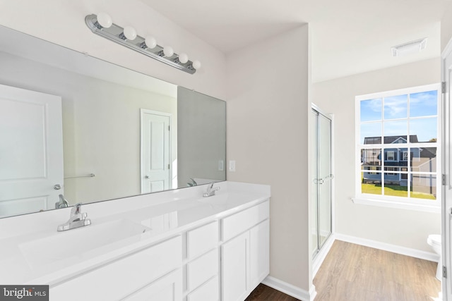 bathroom featuring double vanity, a shower stall, wood finished floors, and a sink