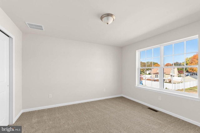 carpeted empty room featuring a wealth of natural light, visible vents, and baseboards