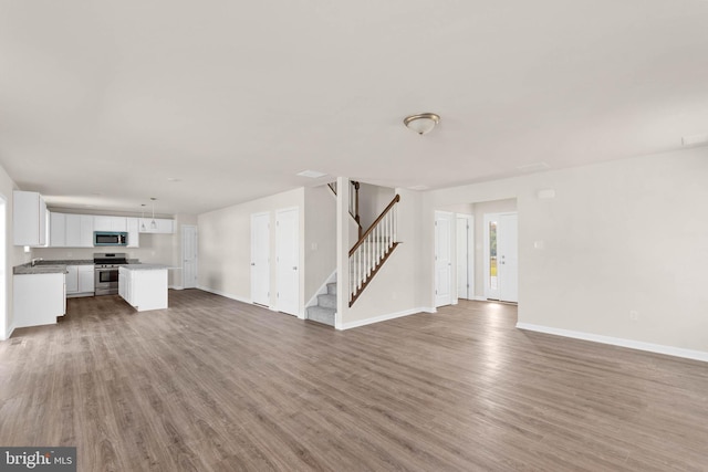 unfurnished living room featuring stairway, wood finished floors, and baseboards