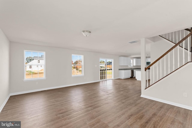 unfurnished living room with visible vents, plenty of natural light, stairway, and wood finished floors