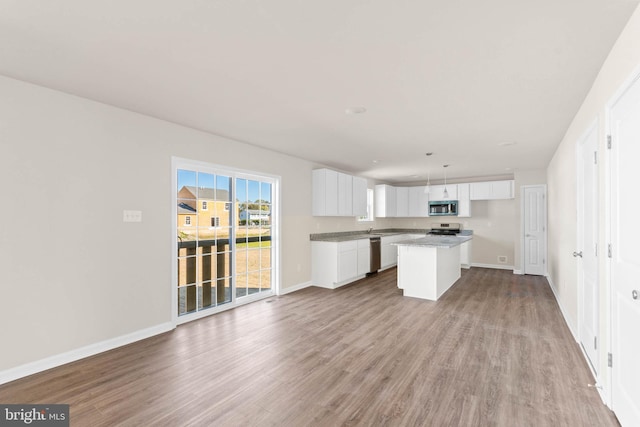 kitchen with wood finished floors, white cabinets, appliances with stainless steel finishes, open floor plan, and a center island