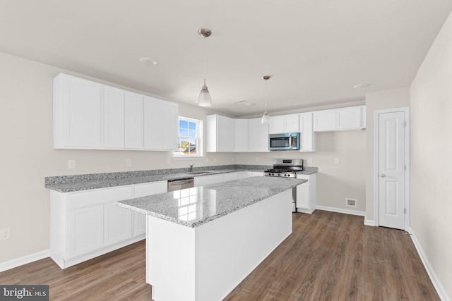 kitchen with a center island, light stone counters, appliances with stainless steel finishes, dark wood-style floors, and white cabinetry