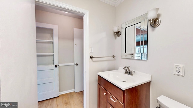 half bathroom featuring toilet, wood finished floors, vanity, and crown molding