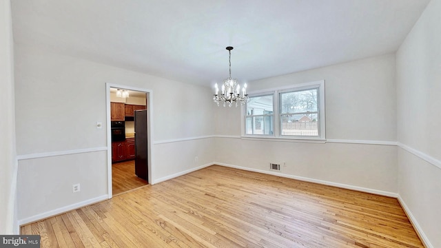 unfurnished dining area featuring a chandelier, visible vents, baseboards, and hardwood / wood-style floors