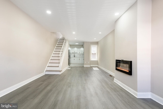 unfurnished living room with a glass covered fireplace, baseboards, and wood finished floors