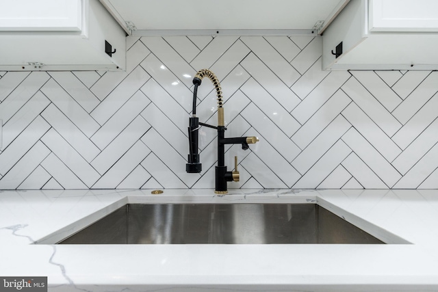 room details featuring a sink, light stone counters, and white cabinetry