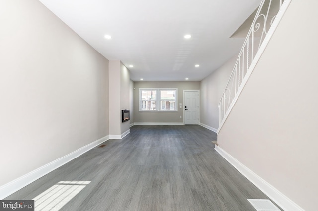 unfurnished living room with dark wood-type flooring, a glass covered fireplace, recessed lighting, baseboards, and stairs