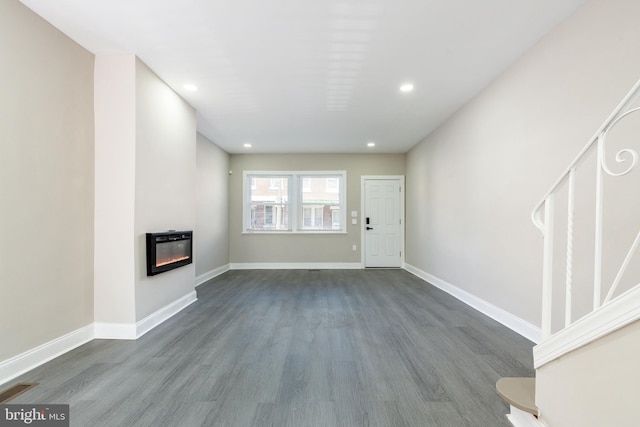 unfurnished living room with visible vents, baseboards, dark wood-style floors, and a glass covered fireplace