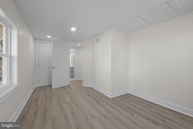 empty room featuring attic access, baseboards, visible vents, and light wood finished floors