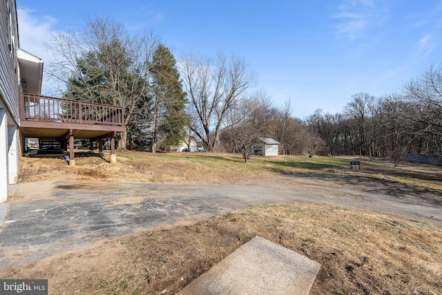 view of yard featuring a deck, aphalt driveway, and an outbuilding