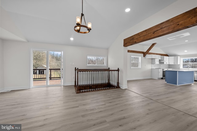 unfurnished living room with a wealth of natural light, light wood-style floors, and vaulted ceiling with beams