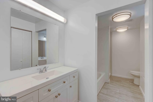 bathroom with a bathing tub, toilet, vanity, and baseboards