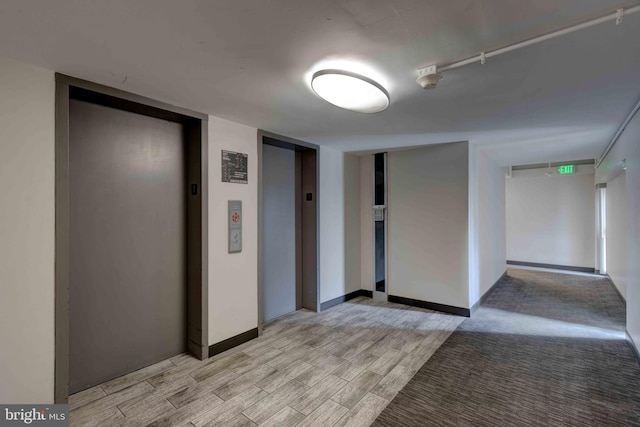 unfurnished room with elevator, light wood-type flooring, and baseboards