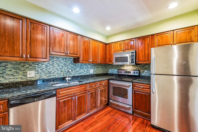 kitchen with dark wood-style floors, a sink, stainless steel appliances, tasteful backsplash, and brown cabinets