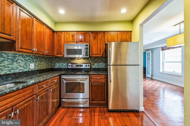 kitchen with backsplash, baseboards, dark wood finished floors, dark stone countertops, and appliances with stainless steel finishes