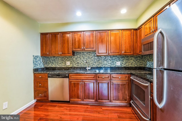 kitchen featuring backsplash, dark wood finished floors, dark stone countertops, appliances with stainless steel finishes, and a sink