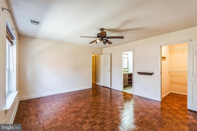 unfurnished bedroom featuring a ceiling fan, baseboards, visible vents, ensuite bath, and a walk in closet