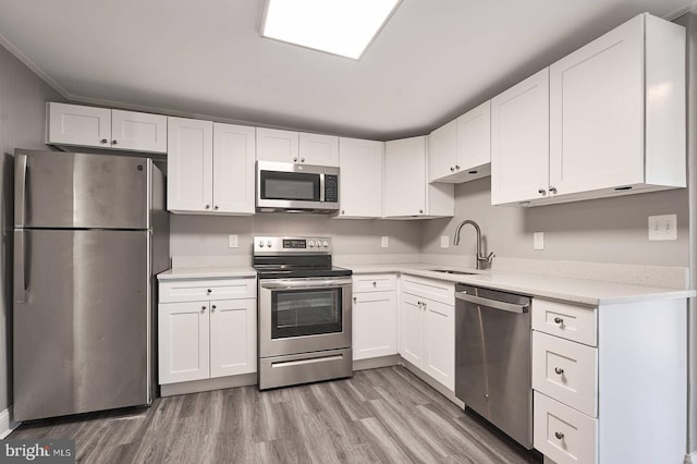 kitchen with white cabinets, stainless steel appliances, light wood-style floors, and a sink