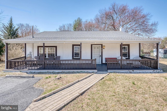 single story home with stucco siding, a front lawn, a porch, roof with shingles, and a chimney