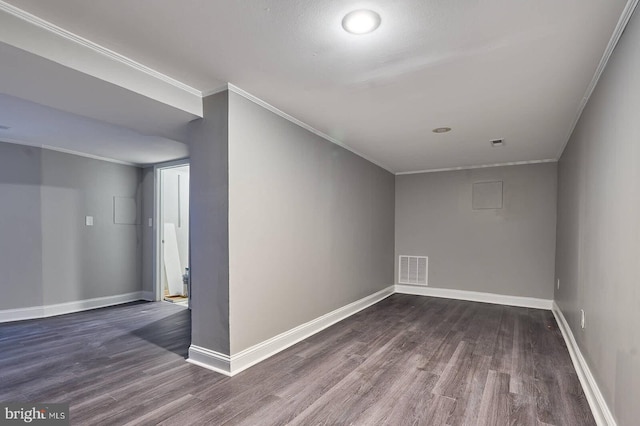 empty room with dark wood finished floors, visible vents, crown molding, and baseboards