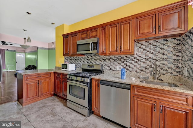 kitchen featuring brown cabinets, a sink, stainless steel appliances, a peninsula, and light stone countertops