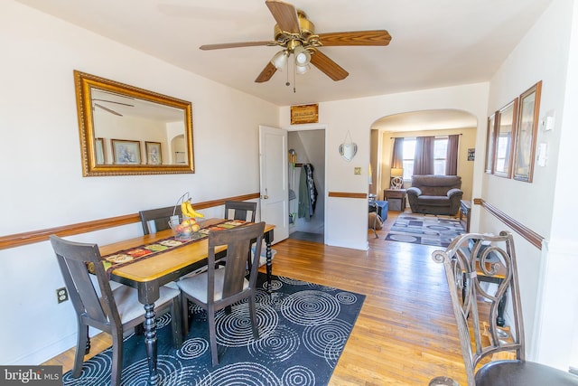 dining area featuring ceiling fan, baseboards, arched walkways, and wood finished floors