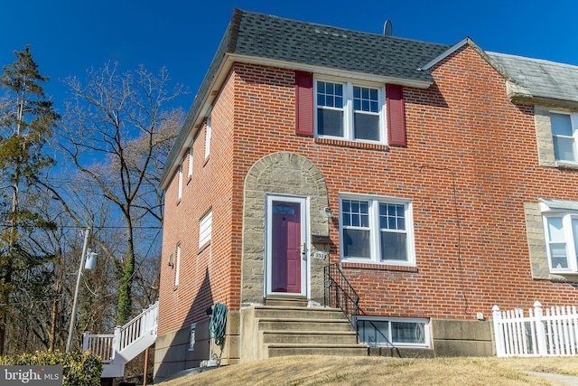 view of front of home featuring fence, brick siding, and roof with shingles