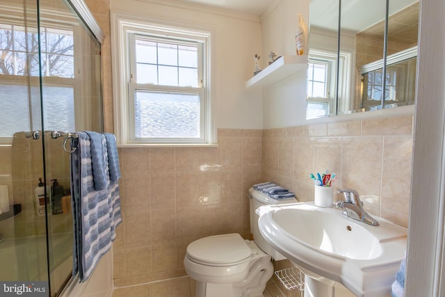 bathroom featuring a shower with door, tile patterned flooring, toilet, tile walls, and a sink