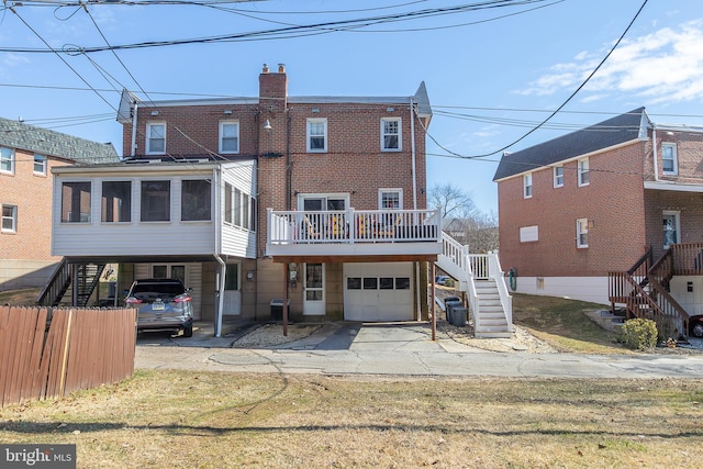 back of property featuring stairway, driveway, an attached garage, a sunroom, and a carport