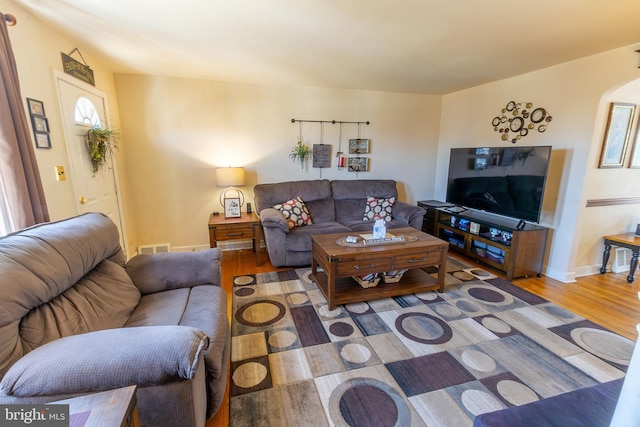 living area with baseboards, arched walkways, visible vents, and wood finished floors