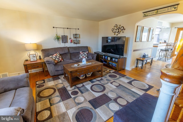 living room with arched walkways, visible vents, baseboards, and wood finished floors