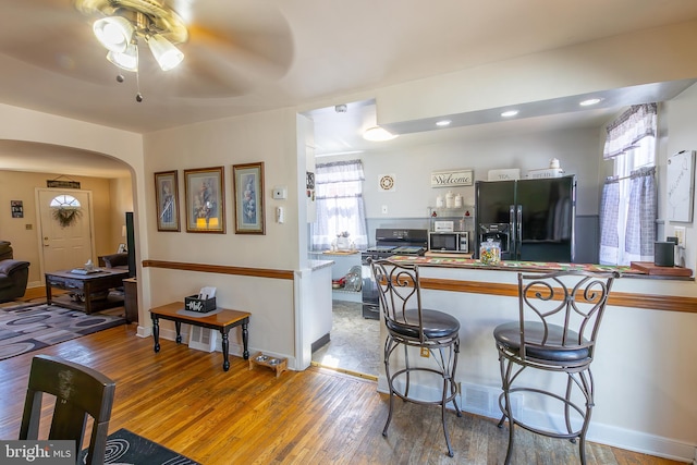 kitchen with wood finished floors, plenty of natural light, arched walkways, stainless steel microwave, and black fridge