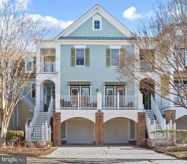 beach home featuring an attached garage, stairs, metal roof, driveway, and a standing seam roof