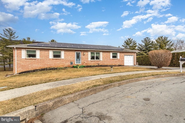 single story home with driveway, a front lawn, an attached garage, brick siding, and solar panels