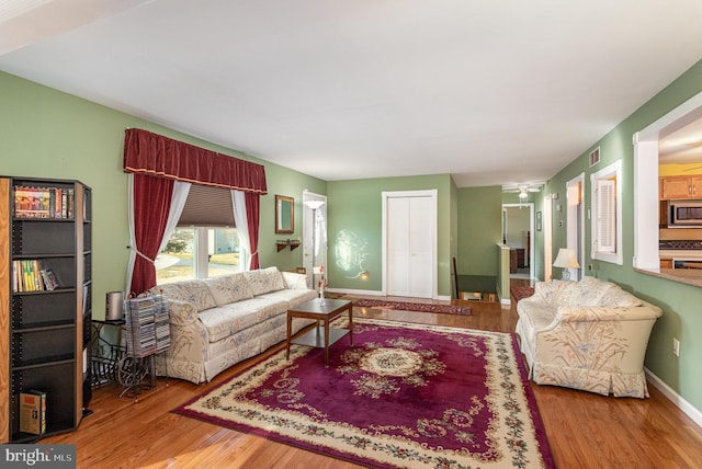 living room featuring ceiling fan, visible vents, baseboards, and wood finished floors